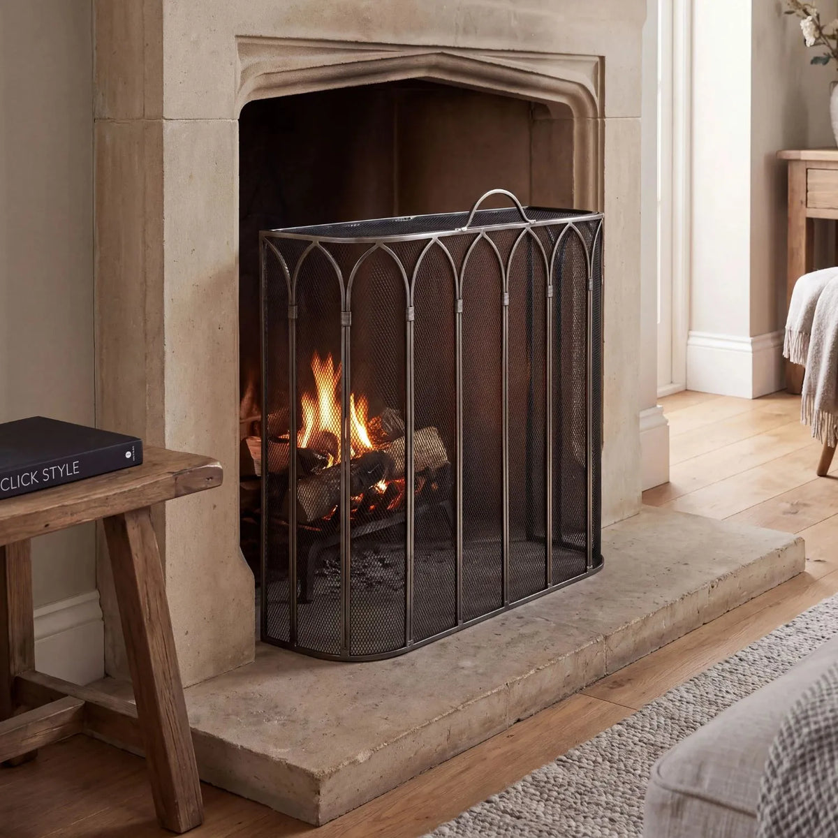 Antique Pewter & Black Firescreen with Top Handle & Gothic Arch Design – Metal Mesh Fireplace Fire Guard 65x55x21cm styled on a stone hearth in front of a traditional fireplace | Click Style