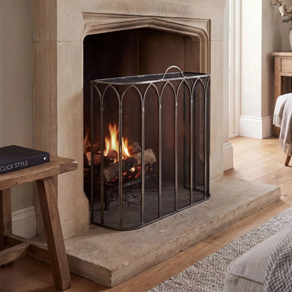 Antique Pewter & Black Firescreen with Top Handle & Gothic Arch Design – Metal Mesh Fireplace Fire Guard 65x55x21cm styled on a stone hearth in front of a traditional fireplace | Click Style