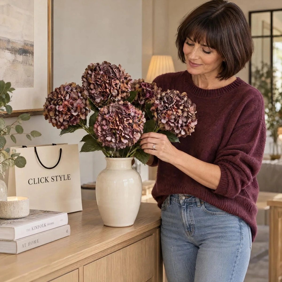 Artificial Antique Mauve & Copper Hydrangea Stem with Burgundy Petals & Realistic Green Leaves – Lifelike Faux Brown Hydrangea Flower 42x18x18cm – Five Artificial Hydrangea Stems Arranged in Cream Vase by Woman Wearing Burgundy Cashmere Jumper | Click Style