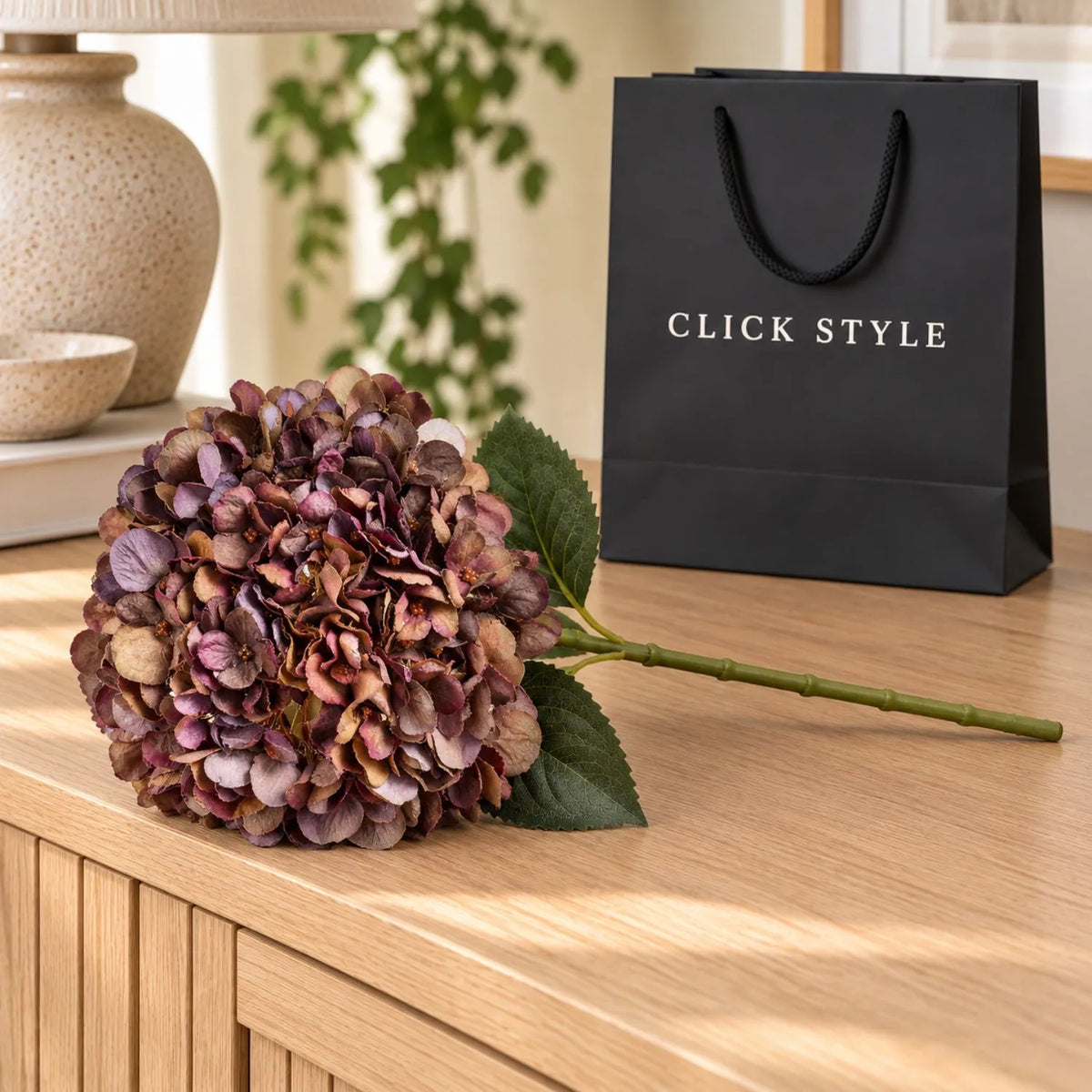 Artificial Antique Mauve & Copper Hydrangea Stem with Burgundy Petals & Realistic Green Leaves – Lifelike Faux Brown Hydrangea Flower 42x18x18cm – Single Stem Displayed on Pale Oak Sideboard with Black Branded Gift Bag | Click Style