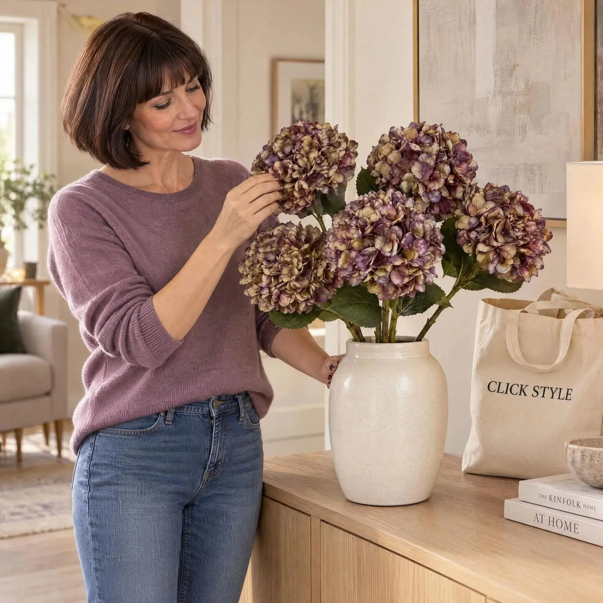 Artificial Burgundy & Plum Hydrangea Stem with Realistic Green Leaves – Lifelike Faux Purple Hydrangea Flower 42x18x18cm – Woman in Mauve Jumper Arranging Five Artificial Hydrangea Stems in Cream Ceramic Vase | Click Style