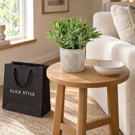 Artificial Green Buxus Plant with Dense Realistic Foliage in Rustic Grey Stone-Effect Pot – Small Faux Potted Plant 20x14x14cm displayed on a round oak side table beside a cream sofa with decorative ceramic bowl and black CLICK STYLE shopping bag | Click Style