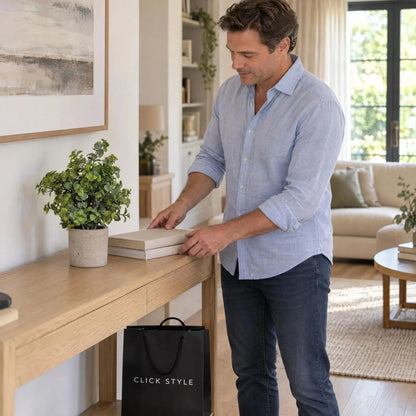 Artificial Green Eucalyptus Plant with Realistic Rounded Leaves in Rustic Stone-Effect Pot – Small Faux Potted Eucalyptus 23x19x19cm displayed on a light oak console table beside a man arranging books in a contemporary living room with black CLICK STYLE shopping bag | Click Style