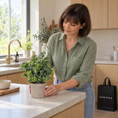 Artificial Green Eucalyptus Plant with Realistic Rounded Leaves in Rustic Stone-Effect Pot – Small Faux Potted Eucalyptus 23x19x19cm being positioned by a woman wearing a green linen shirt on a contemporary kitchen worktop with black CLICK STYLE shopping bag | Click Style