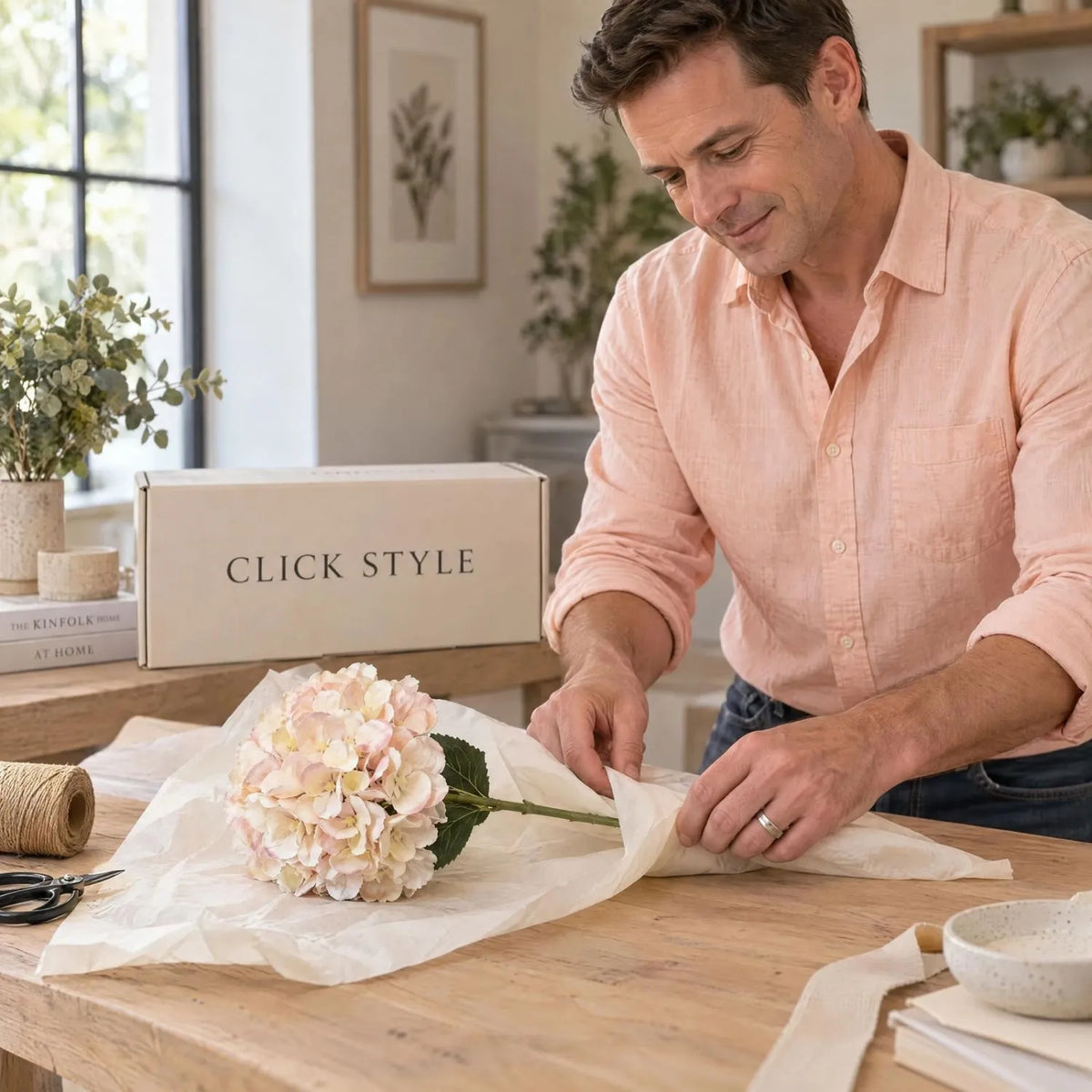 Artificial Peach Blush & Cream Hydrangea Stem with Realistic Green Leaves – Lifelike Faux Pink Hydrangea Flower 42x18x18cm being carefully wrapped in tissue paper by a man wearing a peach shirt beside a CLICK STYLE branded box | Click Style