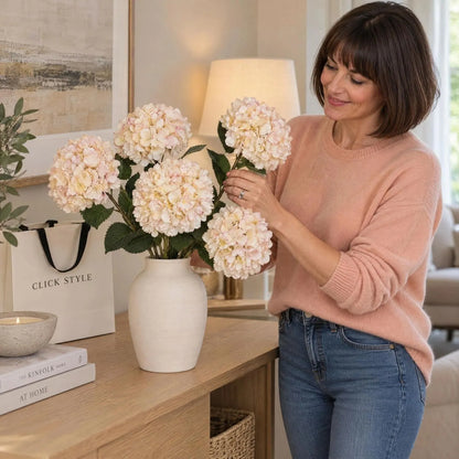Artificial Peach Blush & Cream Hydrangea Stem with Realistic Green Leaves – Lifelike Faux Pink Hydrangea Flower 42x18x18cm shown as five individual stems being arranged in a ceramic vase by a woman wearing a peach cashmere jumper | Click Style