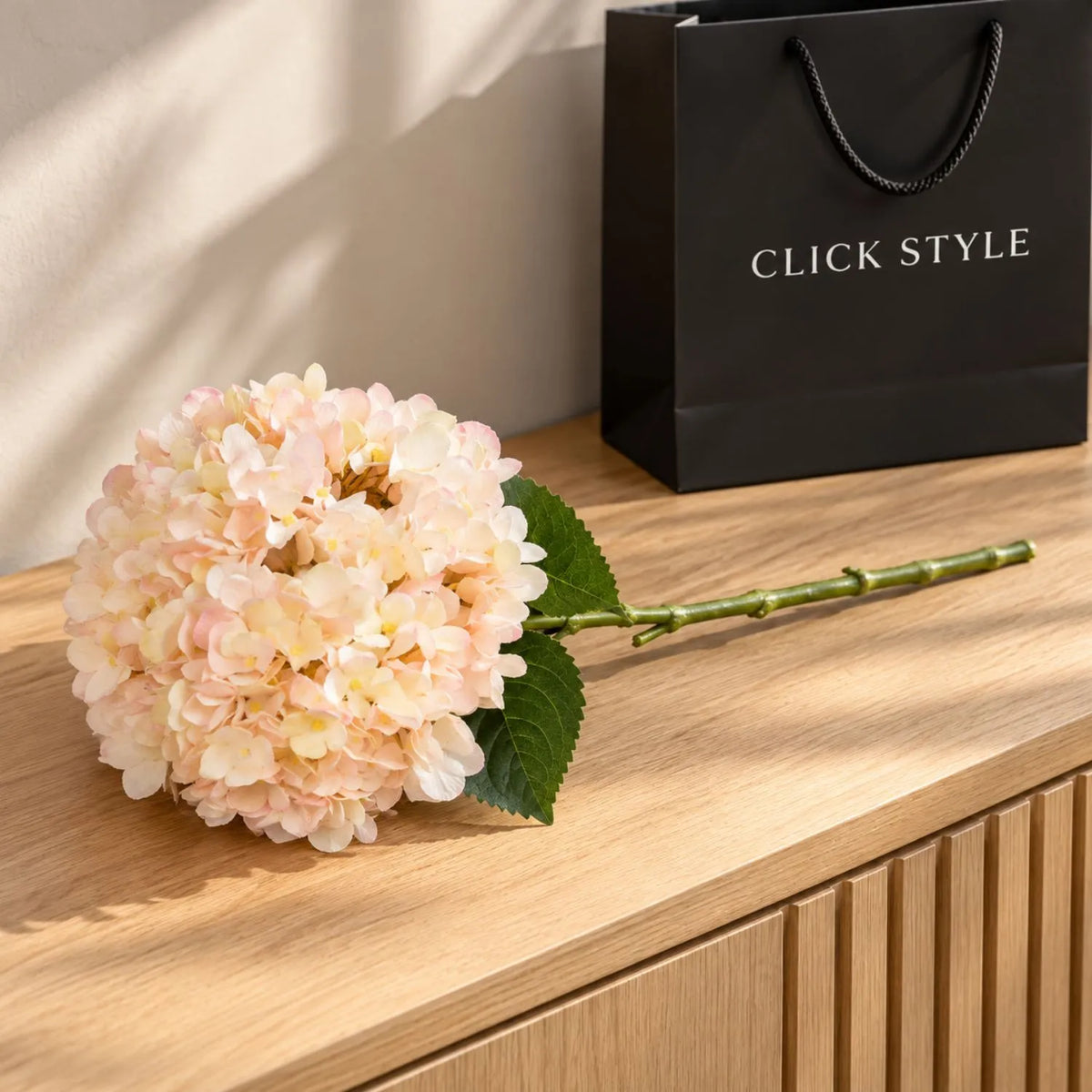 Artificial Peach Blush & Cream Hydrangea Stem with Realistic Green Leaves – Lifelike Faux Pink Hydrangea Flower 42x18x18cm displayed on a pale oak sideboard beside a black CLICK STYLE branded bag | Click Style