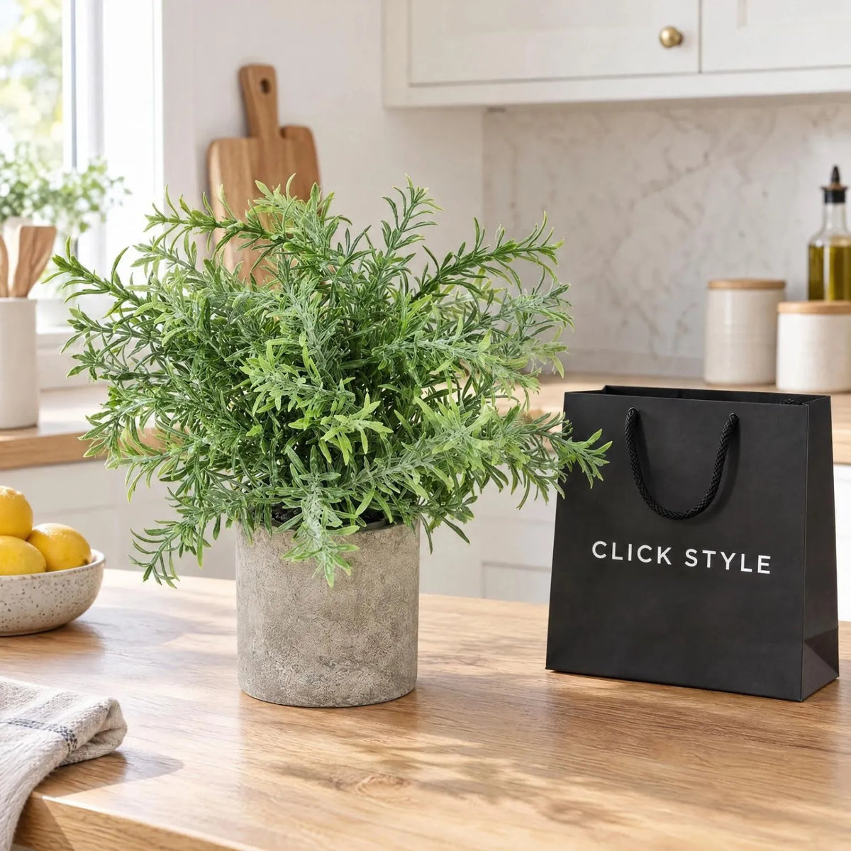 Artificial Rosemary Plant in Grey Stone-Effect Pot with Realistic Green Foliage – Lifelike Faux Potted Herb 24x24x24cm displayed on a light oak kitchen worktop in a contemporary kitchen beside a black shopping bag with white CLICK STYLE branding | Click Style