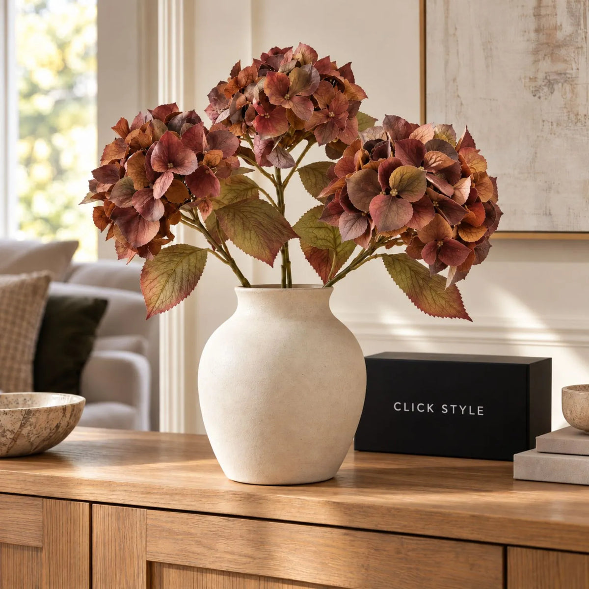 Artificial Russet Brown & Burgundy Hydrangea Stem with Realistic Autumn Foliage – Lifelike Faux Brown Hydrangea Flower 50x26x26cm – Three autumn hydrangea stems arranged in a matt cream ceramic vase on a natural oak sideboard with CLICK STYLE branding | Click Style