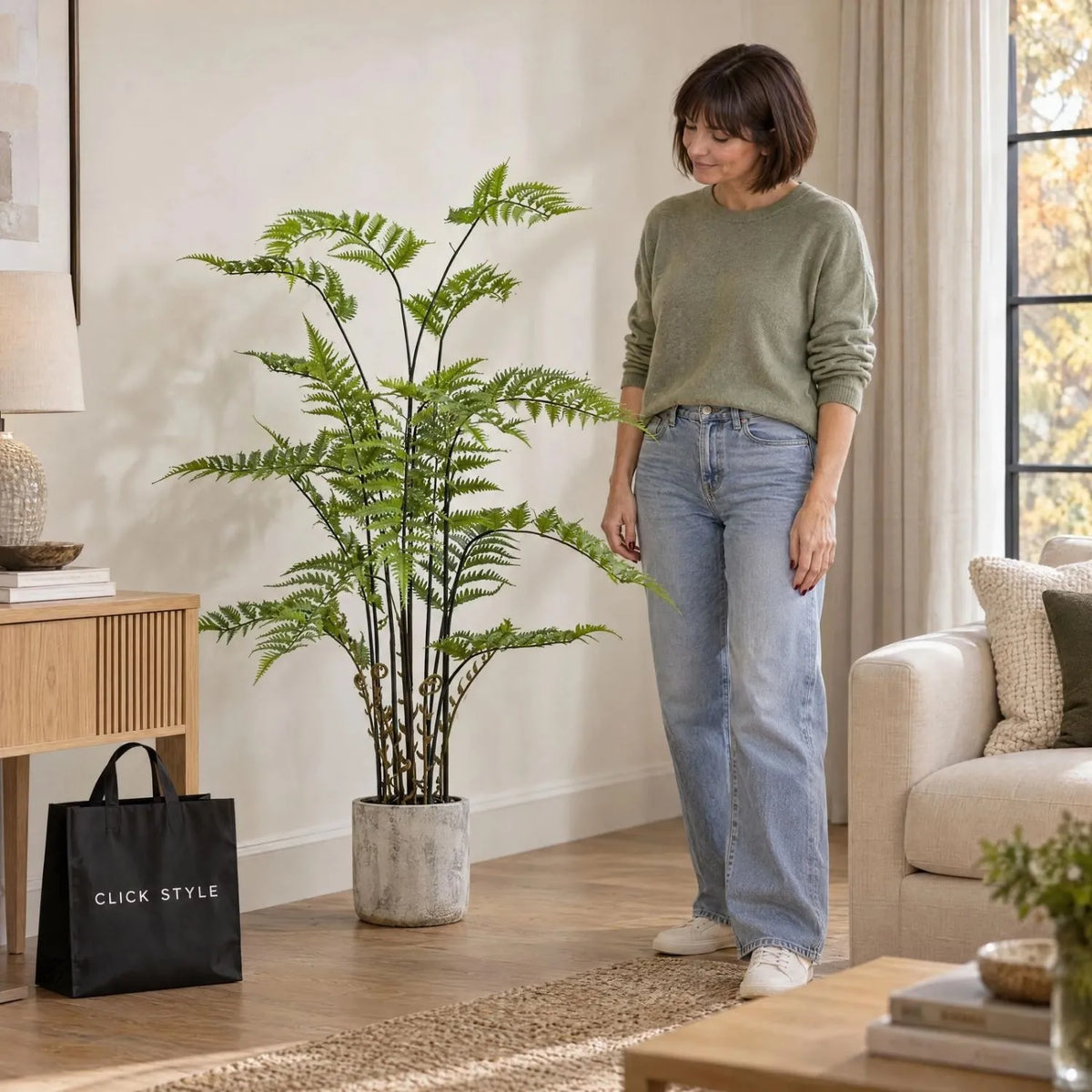 Artificial Tall Green Fern Plant in Distressed Cement Pot with Realistic Fronds – Lifelike Faux Indoor Plant 107x41x41cm displayed beside a woman wearing a green cashmere jumper and light blue jeans in a contemporary living room | Click Style