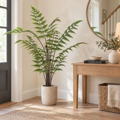 Artificial Tall Green Fern with Delicate Arching Fronds & Brown Fiddleheads in Black Pot – Realistic Floor Standing Faux Fern Plant 120x76x76cm displayed in a cream stone-effect planter with a woman wearing a dark green jumper gently positioning it beside an oak sideboard | Click Style