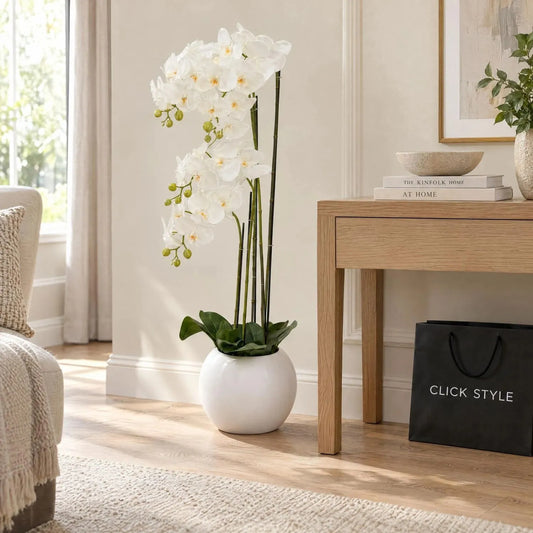 Artificial Tall White Floor Standing Orchid with Cascading Blooms & Green Buds in Round White Ceramic Pot – Realistic Faux Orchid Plant 115x35x35cm styled on a natural oak floor beside a light oak console table in a bright neutral living room with black CLICK STYLE shopping bag | Click Style