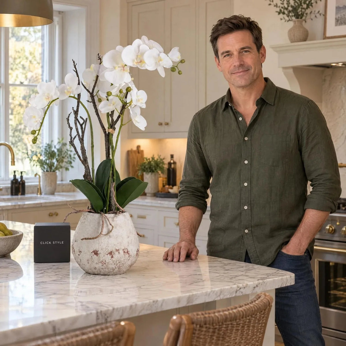 Artificial Tall White Orchid with Cascading Blooms Realistic Exposed Roots & Dark Green Leaves in Weathered Stone Effect Pot – Large Potted Faux Orchid Arrangement 70x46x46cm displayed on a marble kitchen island beside a man wearing an olive-green shirt | Click Style