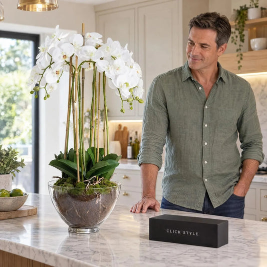 Artificial Tall White Orchid with Cascading Real-Touch Blooms & Exposed Roots in Clear Glass Bowl – Lifelike Faux Potted Orchid Arrangement 88x30x30cm displayed on a marble kitchen island beside a man wearing a sage green shirt with black CLICK STYLE branded box | Click Style