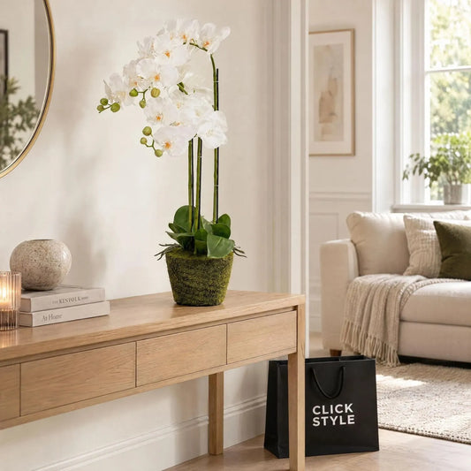 Artificial White Orchid Plant with Cascading Blooms & Green Buds in Moss-Effect Base – Realistic Faux Orchid 80x35x35cm displayed on a light oak console table beside a cream sofa with black CLICK STYLE shopping bag | Click Style
