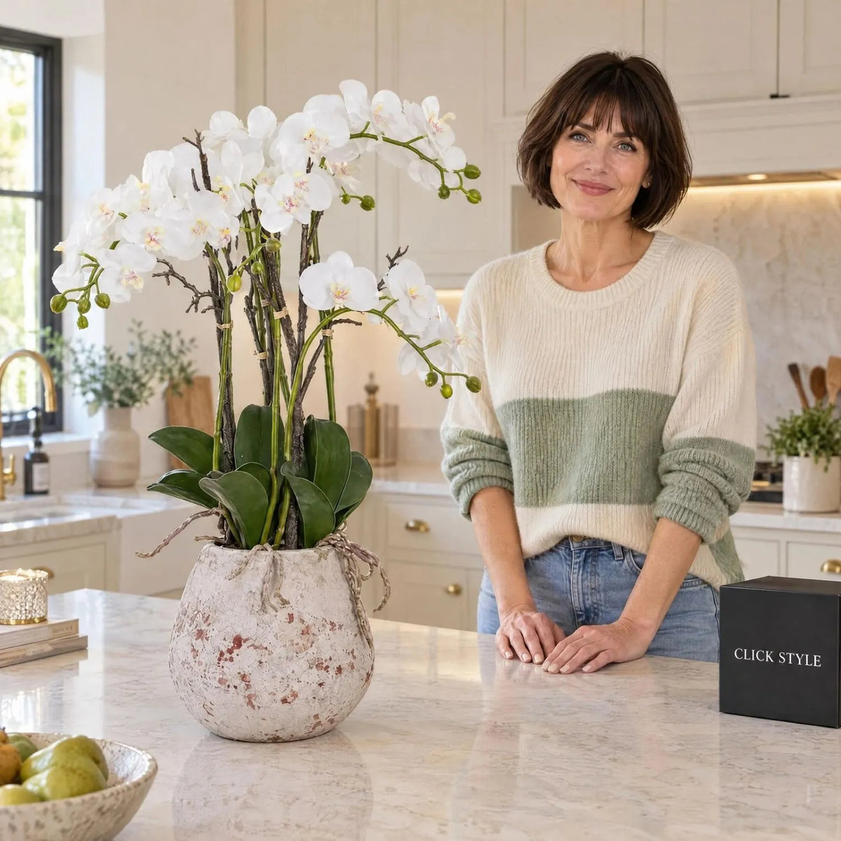 Artificial White Orchid with Cascading Blooms Dark Green Leaves & Realistic Roots in Weathered Stone Effect Pot – Large Potted Faux Orchid Arrangement 70x60x60cm displayed on a luxury kitchen island beside Abbie with black CLICK STYLE presentation box | Click Style