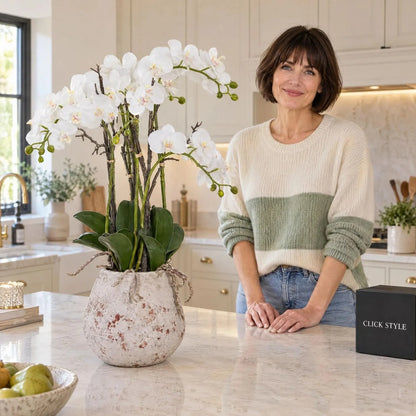 Artificial White Orchid with Cascading Blooms Dark Green Leaves & Realistic Roots in Weathered Stone Effect Pot – Large Potted Faux Orchid Arrangement 70x60x60cm displayed on a luxury kitchen island beside Abbie with black CLICK STYLE presentation box | Click Style