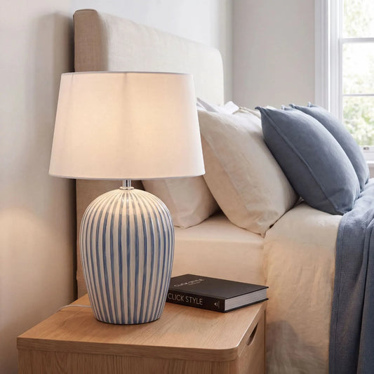Denim Blue & White Striped Ceramic Table Lamp with White Cotton Tapered Shade – Ribbed Bulbous Base Bedside Light 45x30x30cm styled on a wooden bedside table beside a neutral upholstered bed | Click Style
