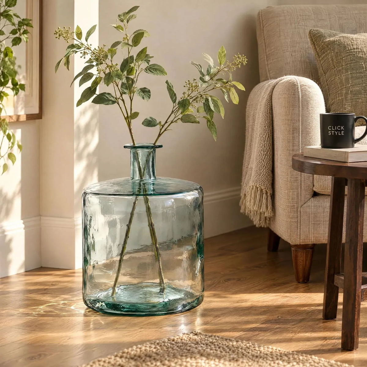Large Clear Recycled Glass Bottle Vase with Narrow Neck – Wide Decorative Floor Vase 45x35x35cm – Styled with Green Foliage Beside a Neutral Armchair | Click Style