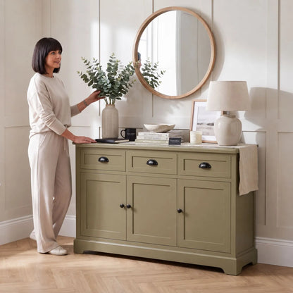Olive Green Pine Wood 3 Door 3 Drawer Sideboard with Matt Black Cup Handles styled in a modern country home with a woman arranging eucalyptus in a ceramic vase 75x120x35cm | Click Style