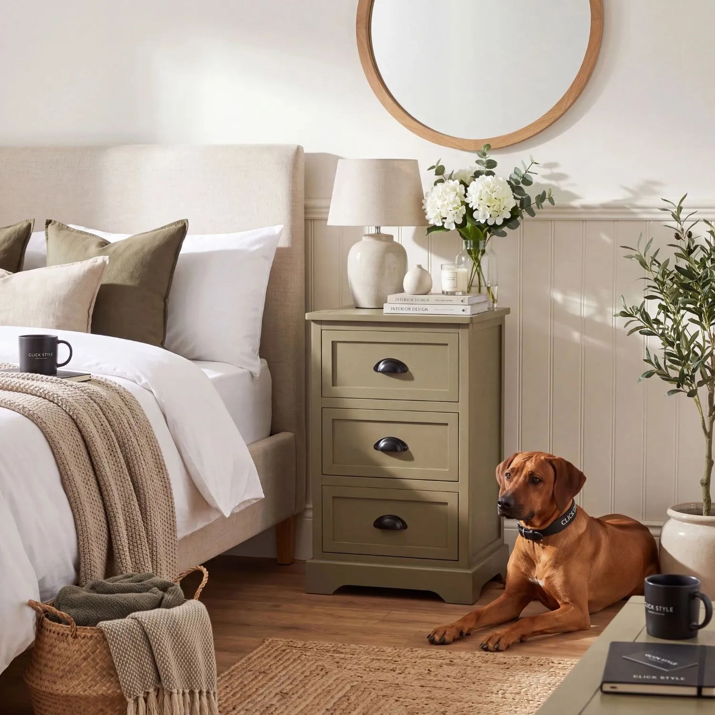 Olive Green Pine Wood 3 Drawer Chest of Drawers with Matt Black Cup Handles Styled as a Bedside Cabinet in a Modern Country Bedroom with Rhodesian Ridgeback Dog 70x41x33cm | Click Style