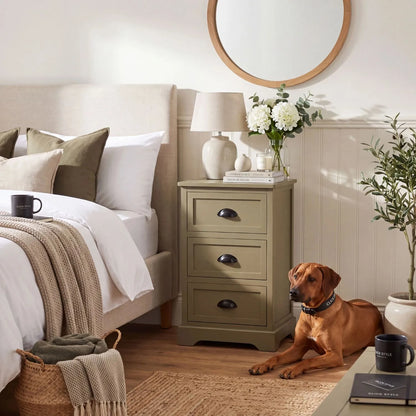 Olive Green Pine Wood 3 Drawer Chest of Drawers with Matt Black Cup Handles Styled as a Bedside Cabinet in a Modern Country Bedroom with Rhodesian Ridgeback Dog 70x41x33cm | Click Style