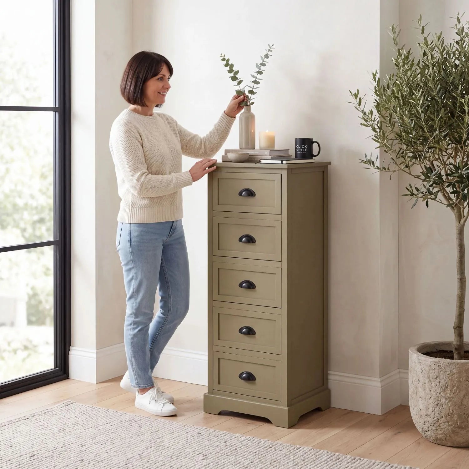 Olive Green Pine Wood 5 Drawer Tall Boy Chest of Drawers with Matt Black Cup Handles styled in a modern country home with a woman arranging eucalyptus stems 108x41x33cm | Click Style