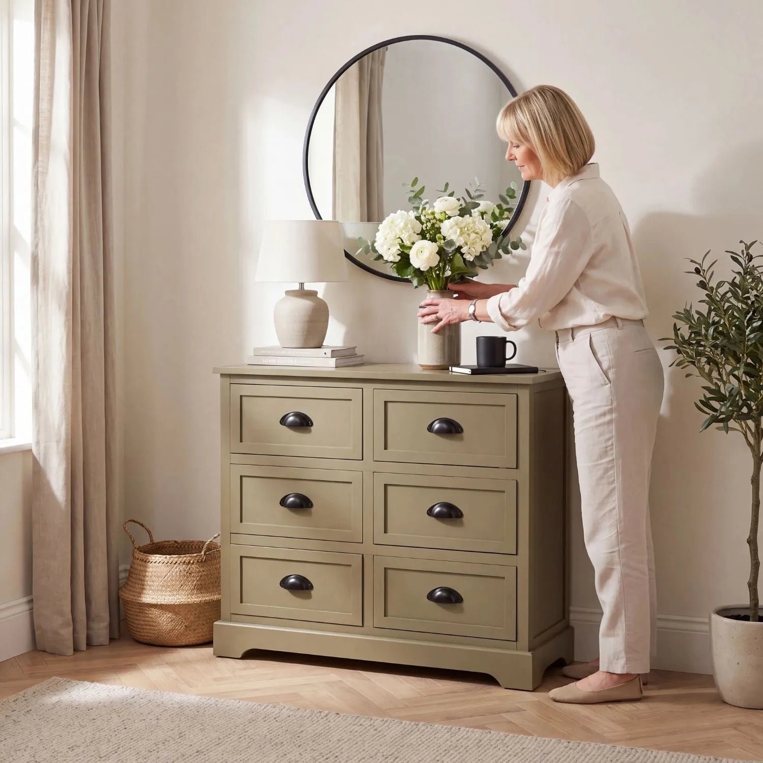 Olive Green Pine Wood 6 Drawer Chest of Drawers with Matt Black Cup Handles Styled in a Modern Country Living Room with Woman Arranging Flowers | Click Style