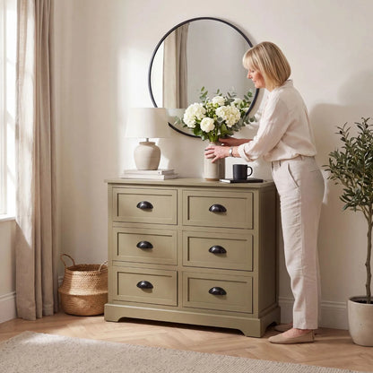 Olive Green Pine Wood 6 Drawer Chest of Drawers with Matt Black Cup Handles Styled in a Modern Country Living Room with Woman Arranging Flowers | Click Style