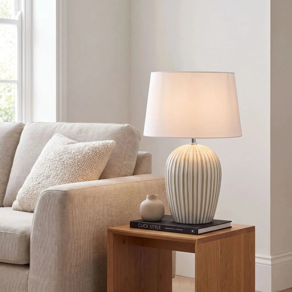 Sage Green & White Striped Ceramic Table Lamp with White Cotton Tapered Shade – Ribbed Bulbous Base Bedside Light 45x30x30cm styled with light on on a natural wood side table beside a neutral sofa | Click Style