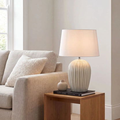 Sage Green & White Striped Ceramic Table Lamp with White Cotton Tapered Shade – Ribbed Bulbous Base Bedside Light 45x30x30cm styled with light on on a natural wood side table beside a neutral sofa | Click Style