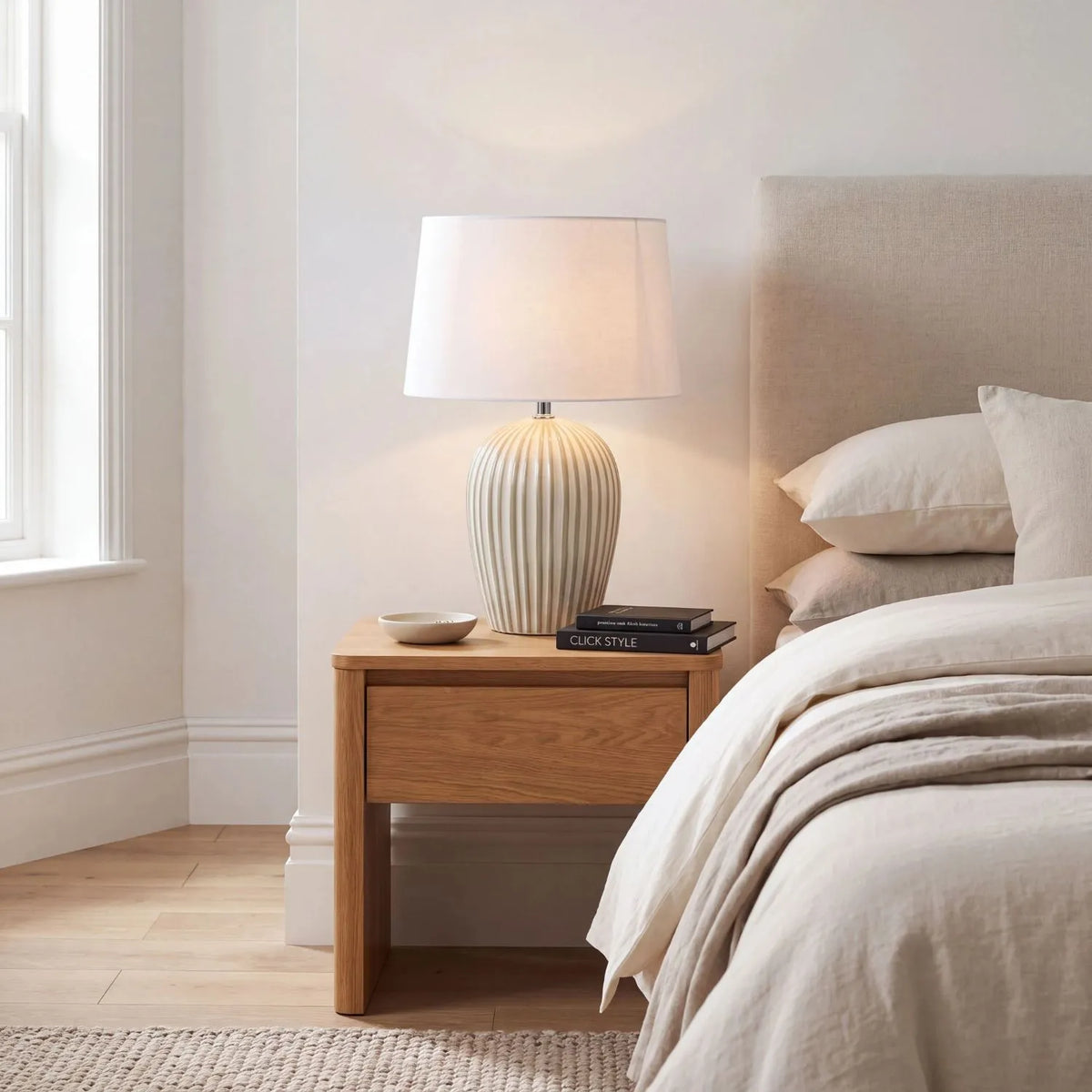 Sage Green & White Striped Ceramic Table Lamp with White Cotton Tapered Shade – Ribbed Bulbous Base Bedside Light 45x30x30cm styled with light on on a natural wood bedside table beside a neutral upholstered bed | Click Style