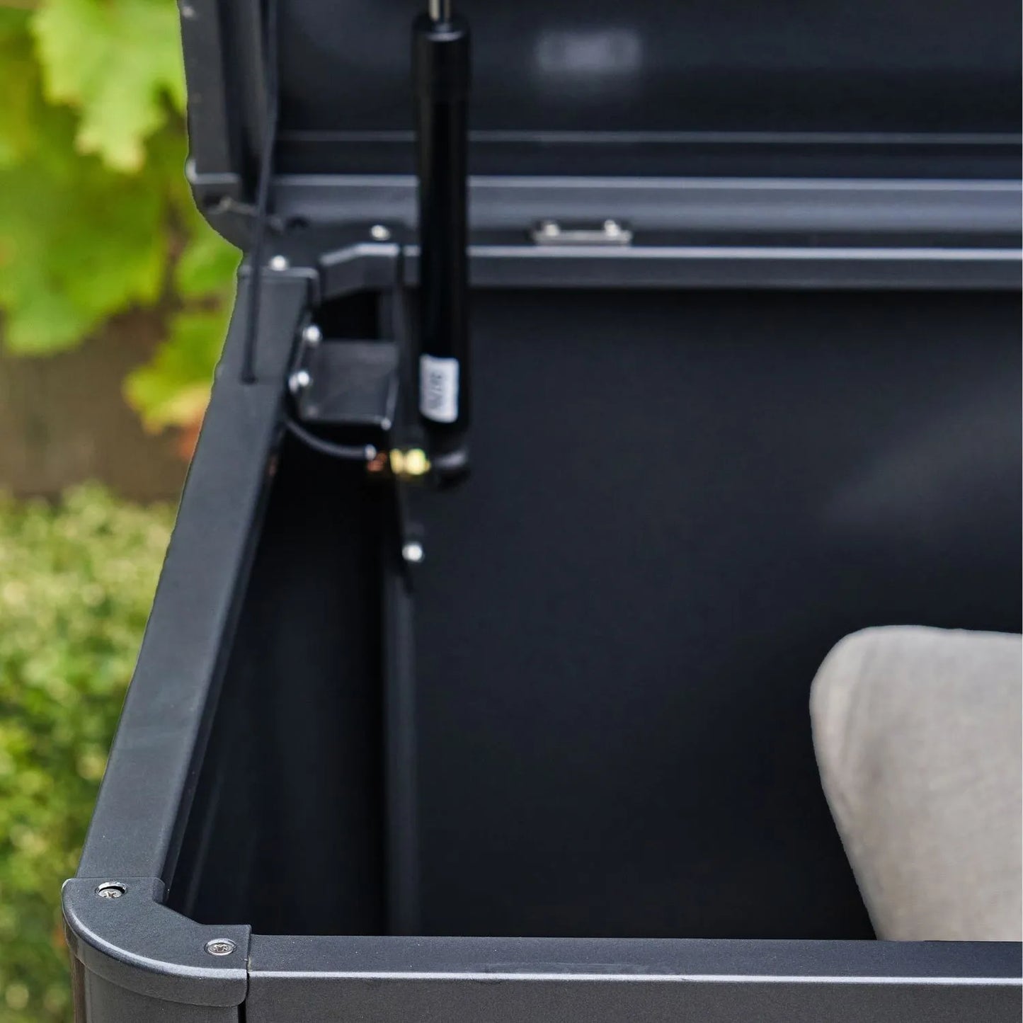 Small Black Galvanised Steel Outdoor Cushion Storage Box lifestyle image from left side with open lid showing gas piston cushion inside and rounded front edge | Click Style