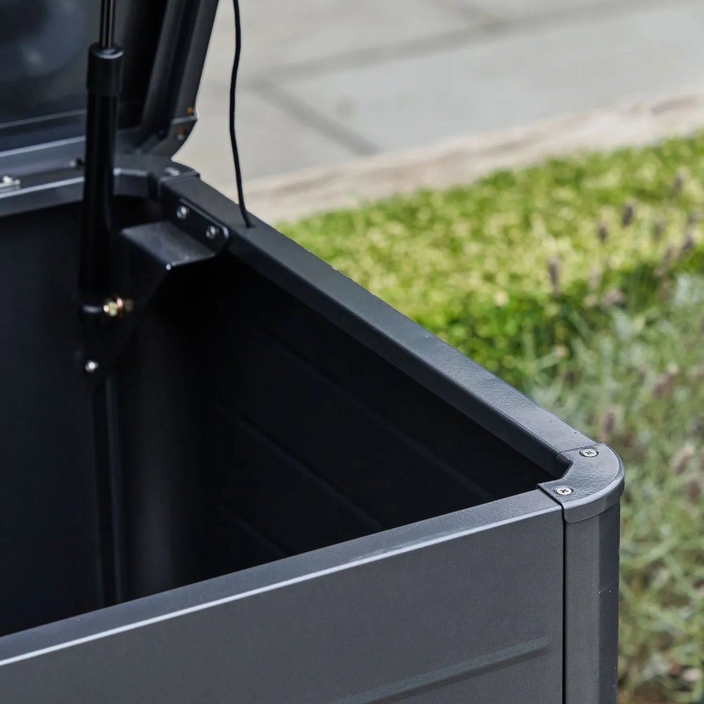 Small Black Galvanised Steel Outdoor Cushion Storage Box lifestyle image from front right with open lid showing gas piston and rounded front edge | Click Style