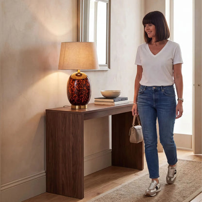 Tall Amber & Brown Tortoiseshell Glass Table Lamp with Natural Linen Tapered Shade styled in a contemporary hallway with a woman 52x33x33cm | Click Style