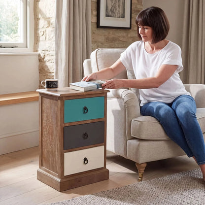 Turquoise blue and neutral distressed pine wood 3 drawer side table with black ring handles styled beside an armchair in a UK living room with woman | Click Style