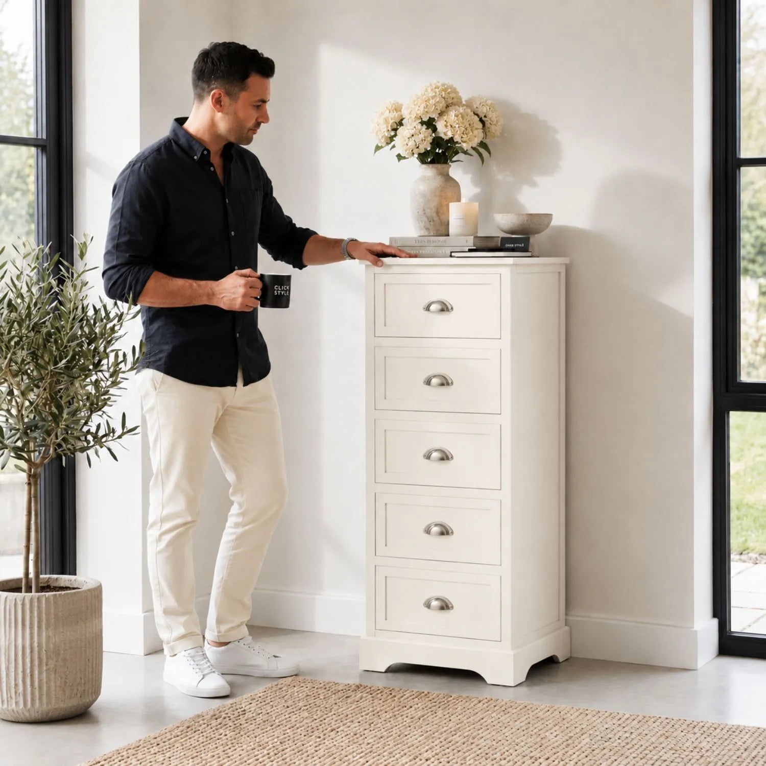 Warm Ivory Pine Wood 5 Drawer Tall Boy Chest of Drawers with Polished Silver Cup Handles styled in a modern home with a man | Click Style