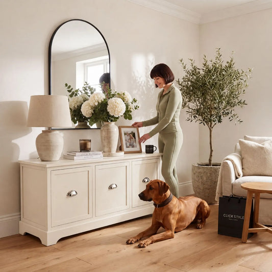 Warm Ivory Pine Wood Low 3 Drawer Storage Unit with Polished Silver Cup Handles styled in a neutral living room with a woman arranging a framed photo and Rhodesian Ridgeback 48x107x39cm | Click Style