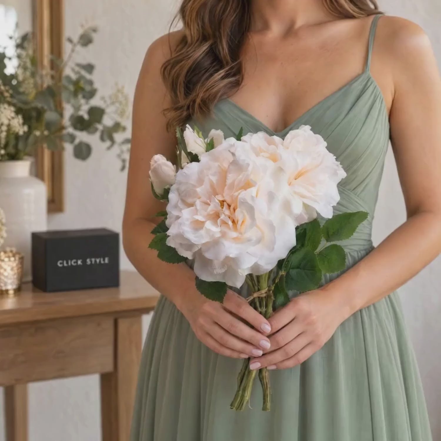 Artificial Pale Peach & Cream Rose Bunch with 3 Twine-Bound Stems – Realistic Faux Peachy Rose Posy 35x25x25cm – Lifestyle video showing a woman in a sage green dress gently holding the pale peach and cream artificial rose bouquet with realistic green foliage and twine-bound stems in a softly lit home interior with CLICK STYLE branded packaging | Click Style