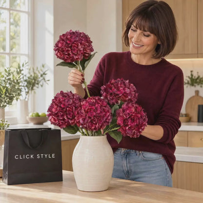 Artificial Deep Ruby Red & Burgundy Hydrangea Stem with Realistic Green Leaves – Lifelike Faux Red Hydrangea Flower 42x18x18cm – Woman in Burgundy Cashmere Jumper Naturally Arranging Five Artificial Hydrangea Stems in a Cream Ceramic Vase on a Kitchen Island with CLICK STYLE Branded Bag | Click Style