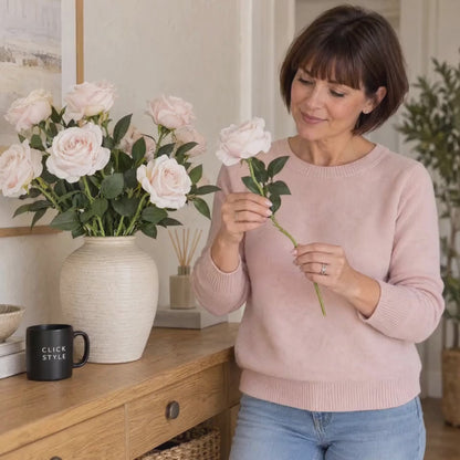 Artificial Pastel Pink Tea Rose Stem with Realistic Green Foliage – Lifelike Pale Pink Faux Rose Flower 53cm – Lifestyle video showing a woman in a pastel pink jumper gently admiring a pale pink artificial rose stem beside a cream ceramic vase filled with matching roses and a black CLICK STYLE branded mug | Click Style
