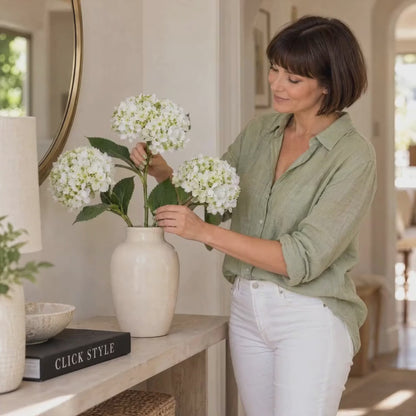 Artificial White Mophead Hydrangea Stem with Full Rounded Bloom & Realistic Green Foliage – Lifelike Faux White Hydrangea Flower 48cm – Woman Finishing a White Hydrangea Arrangement in Cream Ceramic Vase in Lifestyle Video | Click Style