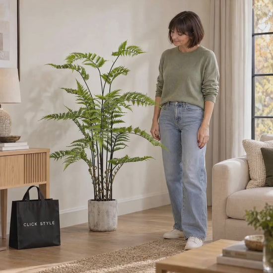 Artificial Tall Green Fern Plant in Distressed Cement Pot with Realistic Fronds – Lifelike Faux Indoor Plant 107x41x41cm – Woman Gently Touching Fern Foliage in Contemporary Living Room | Click Style
