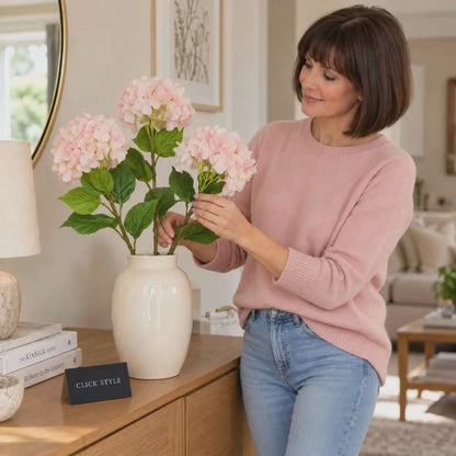 Artificial Soft Pink Long Stem Hydrangea with Full Rounded Flower Head & Realistic Green Leaves – Lifelike Pink Faux Hydrangea Flower 70cm | Lifestyle Video of Woman Arranging Three Soft Pink Hydrangea Stems in an Ivory Ceramic Vase on an Oak Sideboard | Click Style
